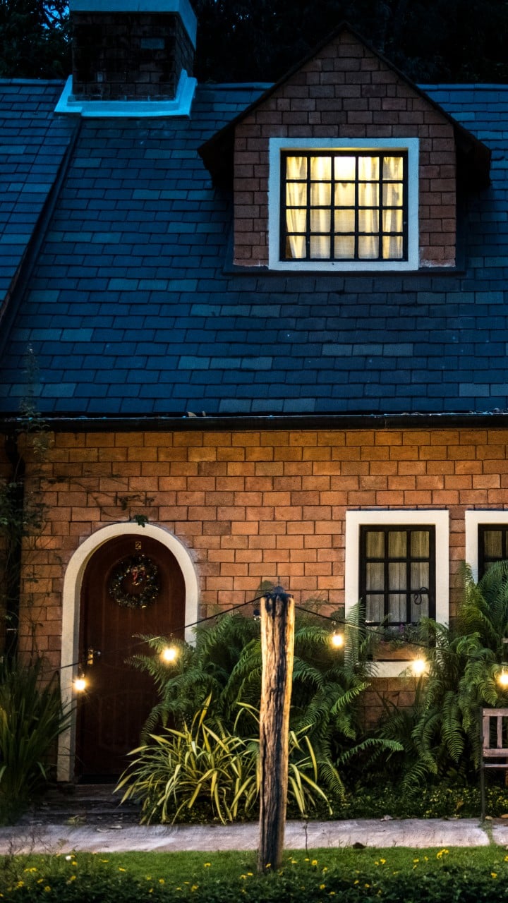 Charming brick house with a lit window and lush greenery at dusk for sale in Carrollton TX